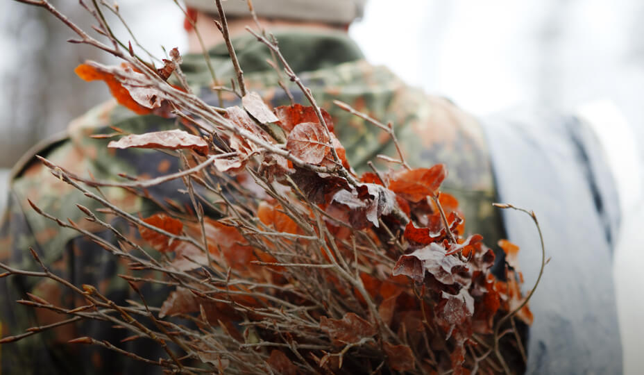 un homme habillé en habit de camouflage porte des branches